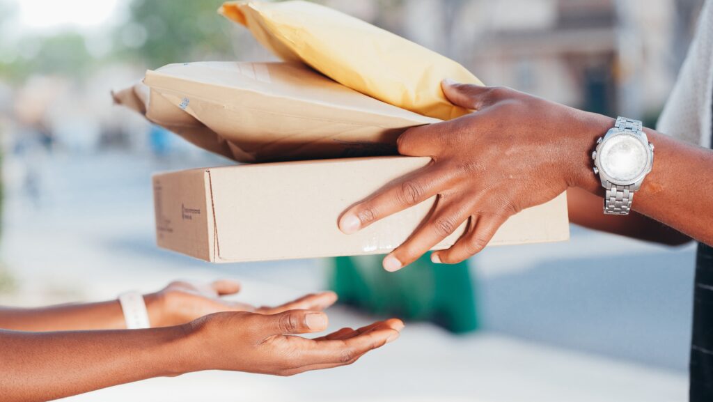 A mailman is handing packages to a customer.